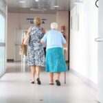 Una donna anziana cammina sostenuta da un familiare all’interno di una struttura sanitaria.