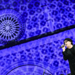 Renato Zero durante la sua esibizione al concerto inaugurale della 731ª Perdonanza Celestiniana, sullo sfondo la facciata illuminata della Basilica di Collemaggio