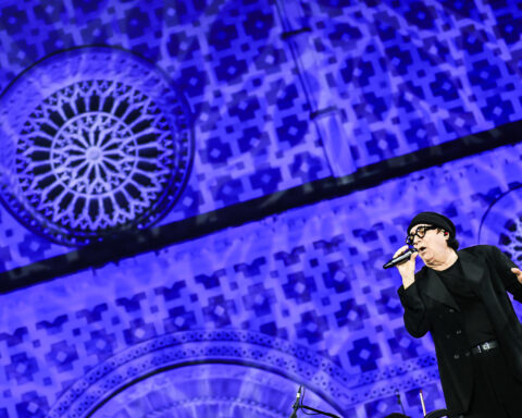 Renato Zero durante la sua esibizione al concerto inaugurale della 731ª Perdonanza Celestiniana, sullo sfondo la facciata illuminata della Basilica di Collemaggio