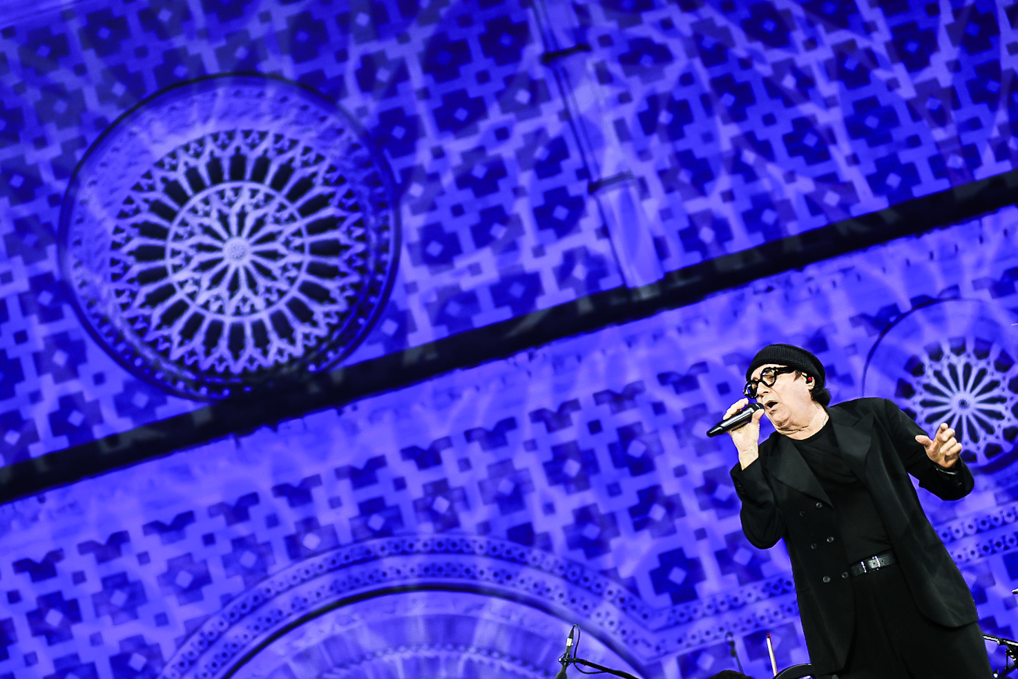 Renato Zero durante la sua esibizione al concerto inaugurale della 731ª Perdonanza Celestiniana, sullo sfondo la facciata illuminata della Basilica di Collemaggio