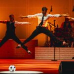 Stefano De Martino durante una coreografia di “Meglio Stasera Summer Tour 2025”, accompagnato dai ballerini e dalla Disperata Erotica Band