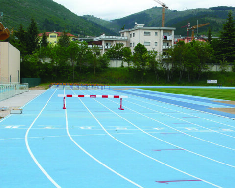 Vista sulle tribune e sulla pista di atletica color azzurro, immersa in uno scenario montano, con impianti e spalti recentemente rinnovati per ospitare allenamenti e competizioni.