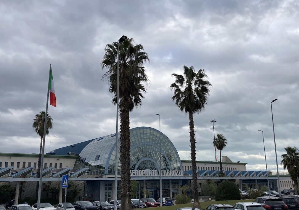 aeroporto d'Abruzzo, nel parcheggio ci sono due palme, le macchine dei passeggeri e d'edificio dell'aeroporto