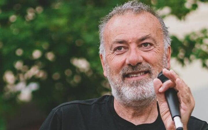 Franco Arminio, poeta e scrittore in primo piano con un microfono in una mano e con un albero sullo sfondo