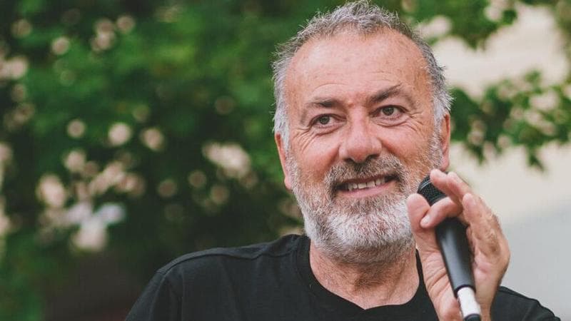 Franco Arminio, poeta e scrittore in primo piano con un microfono in una mano e con un albero sullo sfondo