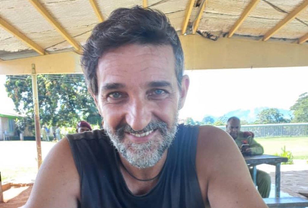 un uomo, carlo d'attanasio, sorride all'aria aperta. si trova sotto un capanno e si intravedono dei soldati stranieri