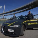 Guardia di Finanza, due finanzieri e un'auto di ordinanza. Sullo sfondo il ponte del mare