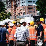 Operai e tecnici in cantiere con caschetti e giubbotti arancioni, simbolo del mondo del lavoro in Abruzzo. L’immagine richiama il tema della precarietà e della crisi occupazionale al centro dello scontro politico.