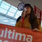 Un’attivista di “Ultima Generazione” con megafono e striscione arancione durante la protesta nel supermercato Conad dell’Aquila contro precarietà e salari bassi.