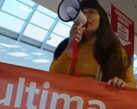 Un’attivista di “Ultima Generazione” con megafono e striscione arancione durante la protesta nel supermercato Conad dell’Aquila contro precarietà e salari bassi.