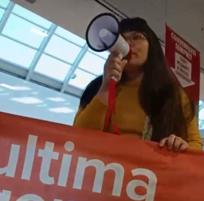 Un’attivista di “Ultima Generazione” con megafono e striscione arancione durante la protesta nel supermercato Conad dell’Aquila contro precarietà e salari bassi.
