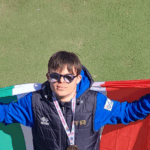 L’atleta abruzzese Nando D’Agostino festeggia la medaglia d’oro ai Mondiali FISDIR di atletica leggera a Brisbane, sventolando la bandiera italiana sul podio. Il giovane marciatore della Polisportiva Tethys di Chieti ha conquistato il titolo iridato nei 1500 metri.