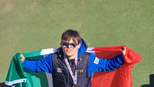 L’atleta abruzzese Nando D’Agostino festeggia la medaglia d’oro ai Mondiali FISDIR di atletica leggera a Brisbane, sventolando la bandiera italiana sul podio. Il giovane marciatore della Polisportiva Tethys di Chieti ha conquistato il titolo iridato nei 1500 metri.