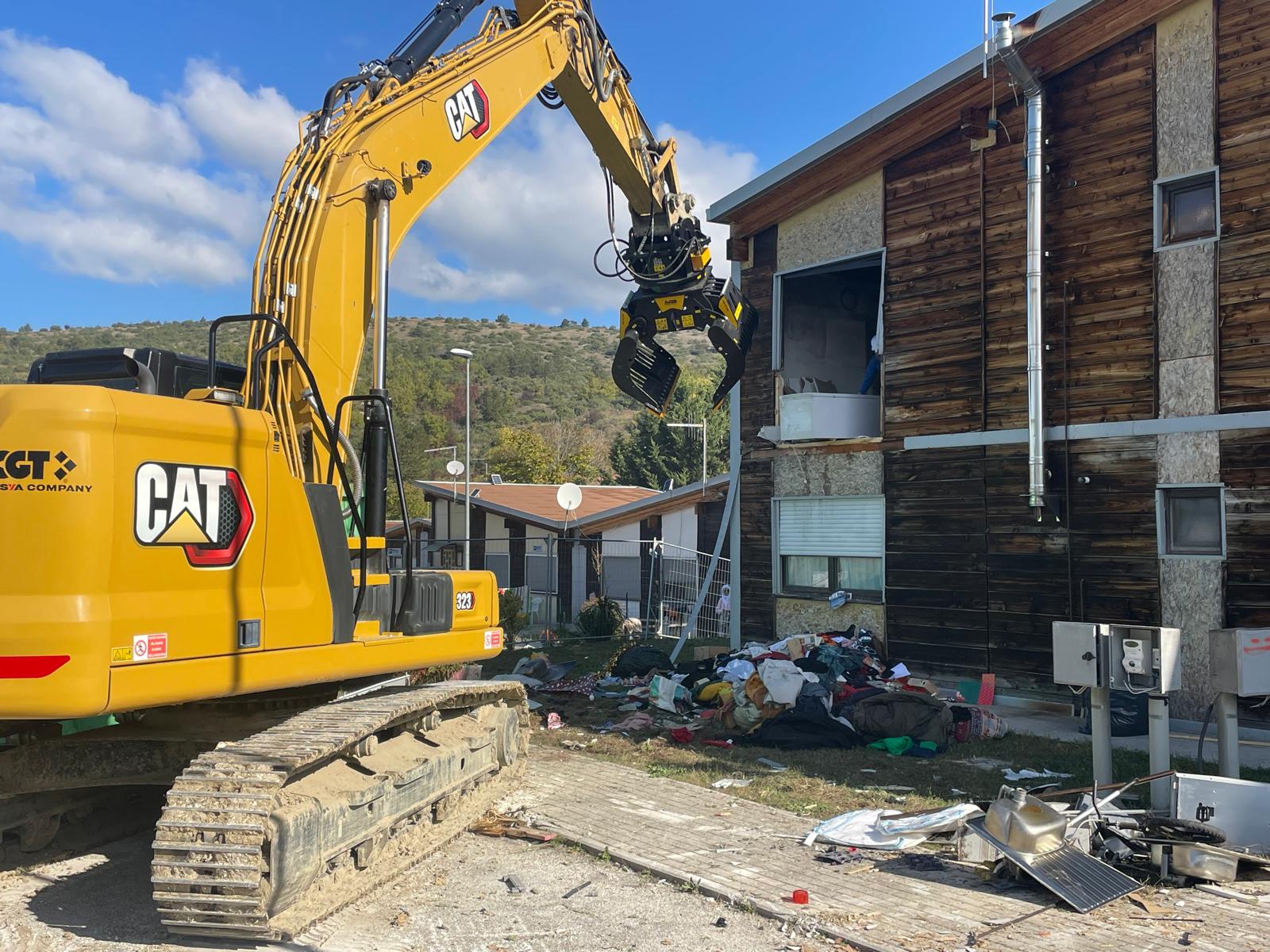 Escavatore in azione nel villaggio Map di San Gregorio, dove sono iniziati gli interventi di demolizione di dieci alloggi inutilizzati