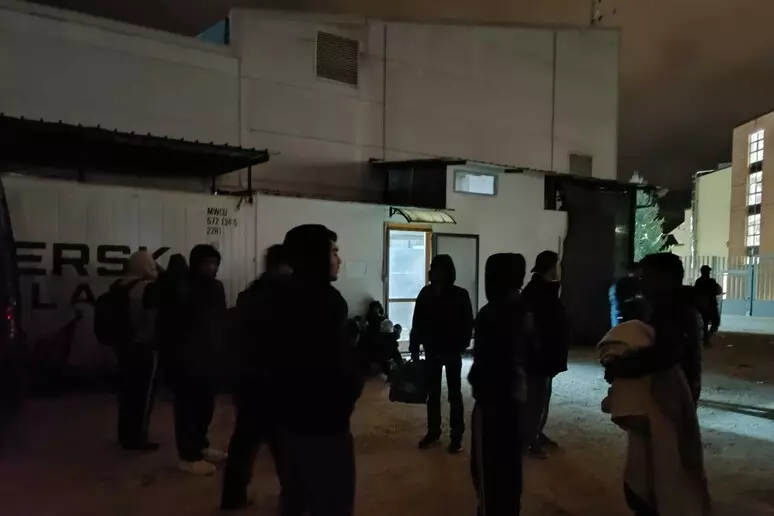 Gruppi di migranti raccolti nei pressi della Questura dell’Aquila, dove molti trascorrono la notte all’aperto dopo la rimozione di coperte e cartoni segnalata dai residenti