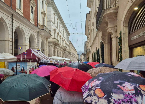 Ombrelli aperti lungo il percorso della Fiera dell’Epifania nel centro storico dell’Aquila, segnata dal maltempo. Nonostante la pioggia battente, cittadini e visitatori non rinunciano alla tradizionale passeggiata tra le bancarelle.