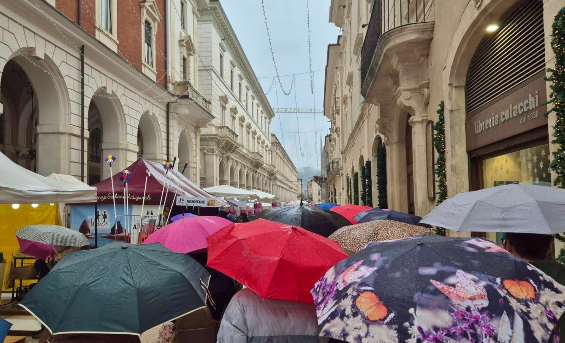 Ombrelli aperti lungo il percorso della Fiera dell’Epifania nel centro storico dell’Aquila, segnata dal maltempo. Nonostante la pioggia battente, cittadini e visitatori non rinunciano alla tradizionale passeggiata tra le bancarelle.